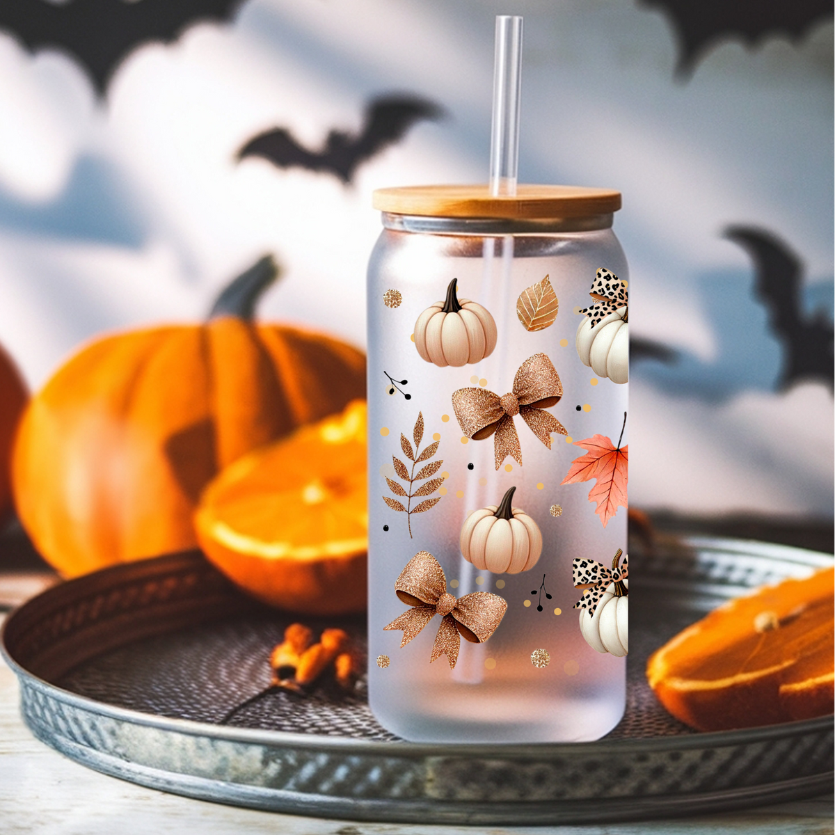 A frosted glass tumbler with a bamboo lid and clear straw, decorated with autumn motifs including pumpkins, leaves, and bows, displayed on a tray with pumpkins and bats in the background.