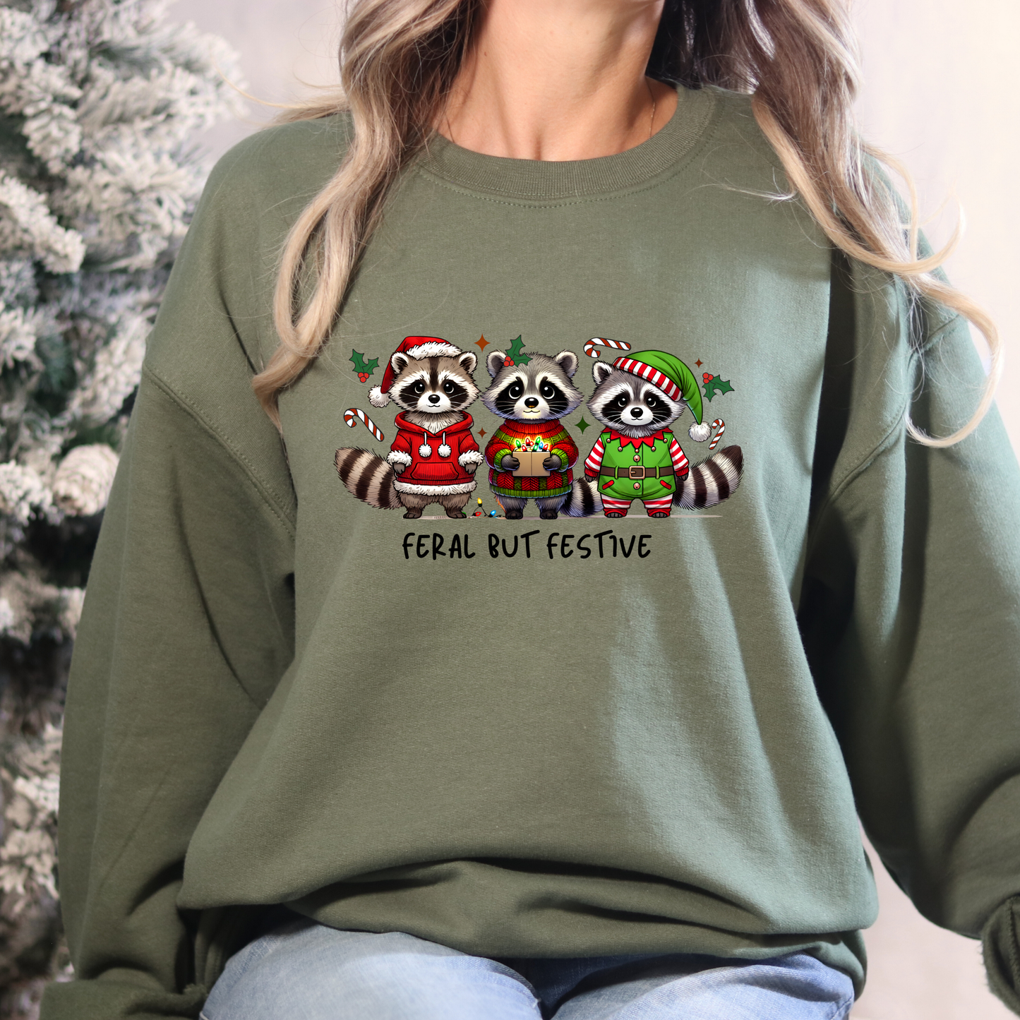 Person wearing a green sweatshirt with Christmas-themed raccoon design and text 'Feral But Festive'.