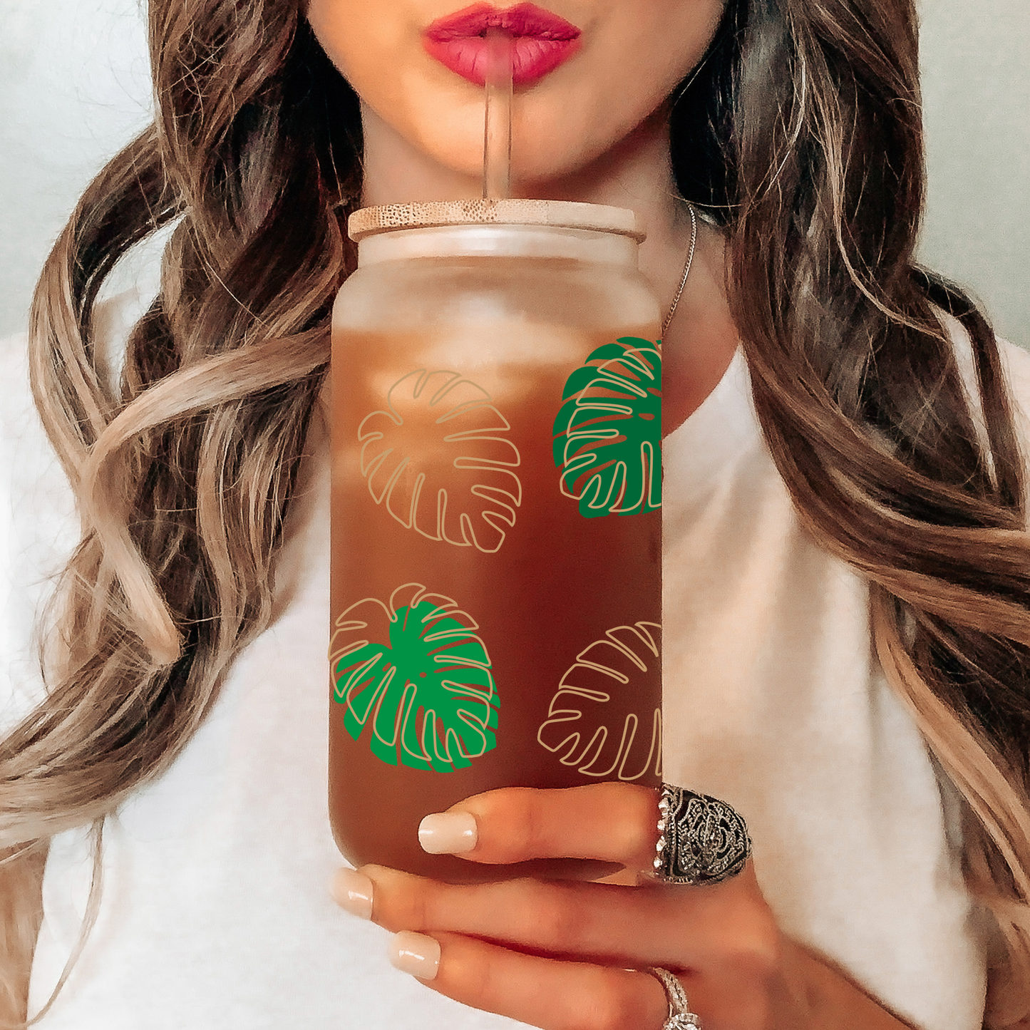 Person holding a tumbler with green leaf patterns, drinking from it.
