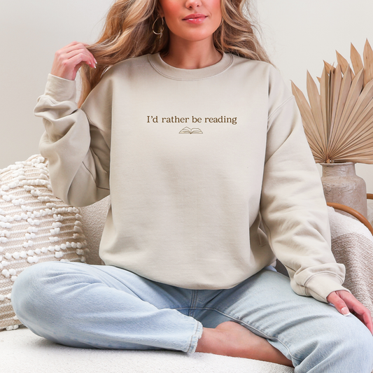 Person wearing a beige sweatshirt with 'I'd rather be reading' text, sitting on a couch.