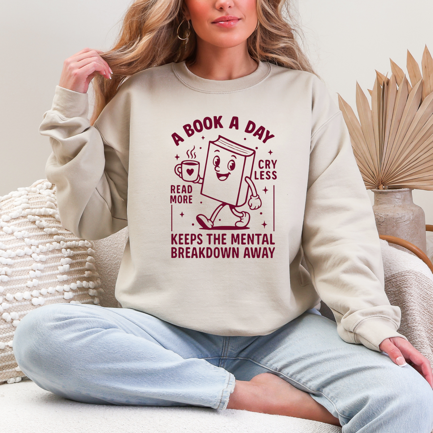 Person wearing a beige sweatshirt with a book-themed design, sitting on a couch.