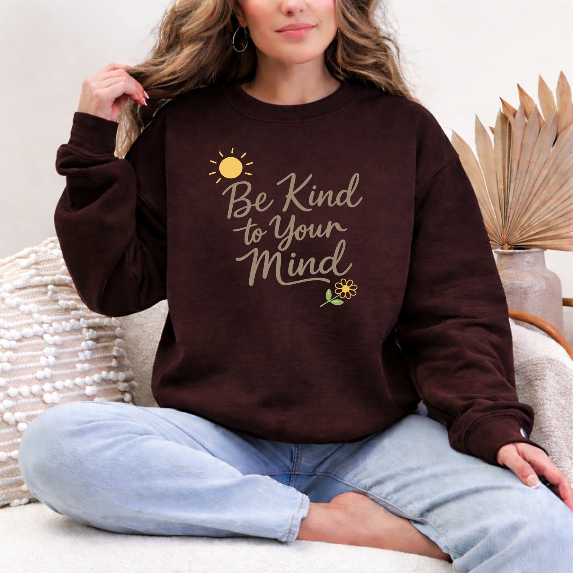 Person wearing a brown sweatshirt with 'Be Kind to Your Mind' text, sitting on a couch.