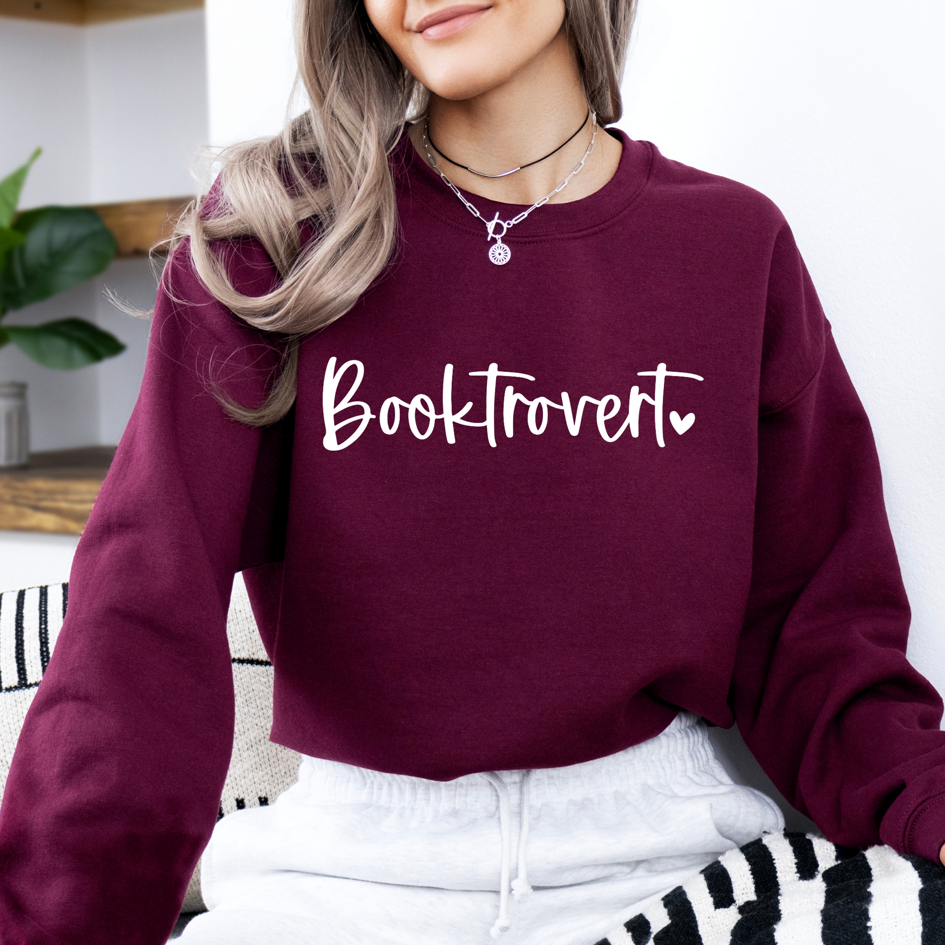 Person wearing a maroon sweatshirt with 'Booktrovert' text, sitting on a striped couch.