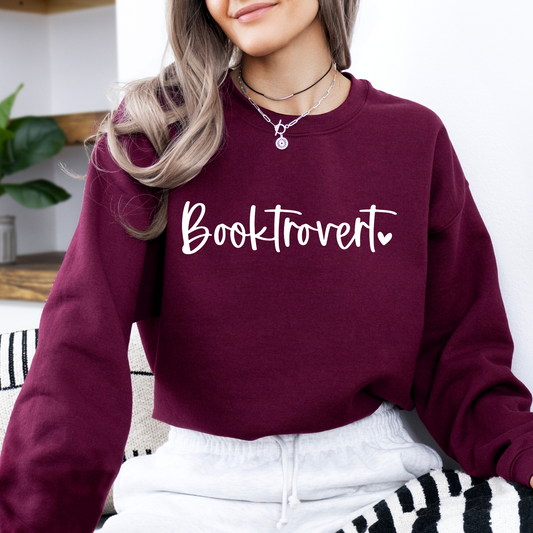 Person wearing a maroon sweatshirt with 'Booktrovert' text, sitting on a striped couch.