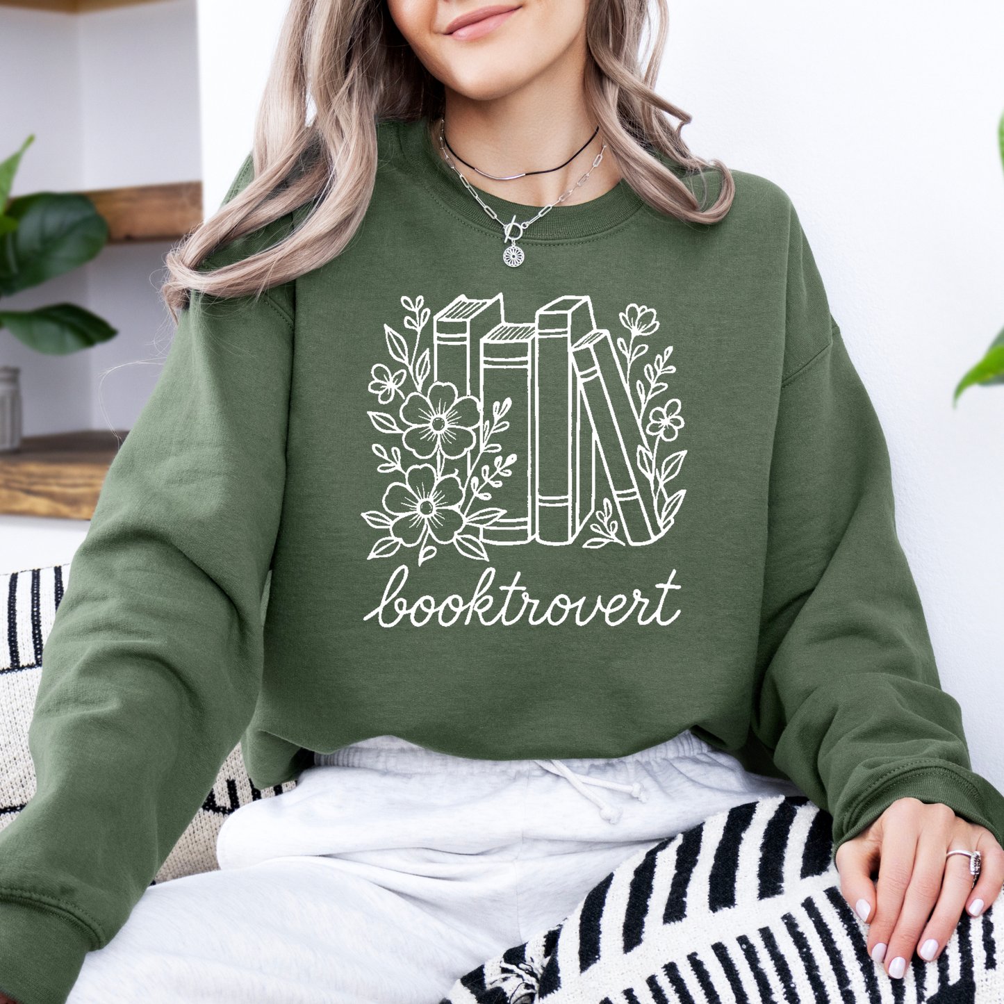 Person wearing a green sweatshirt with 'booktrovert' design and books illustration.