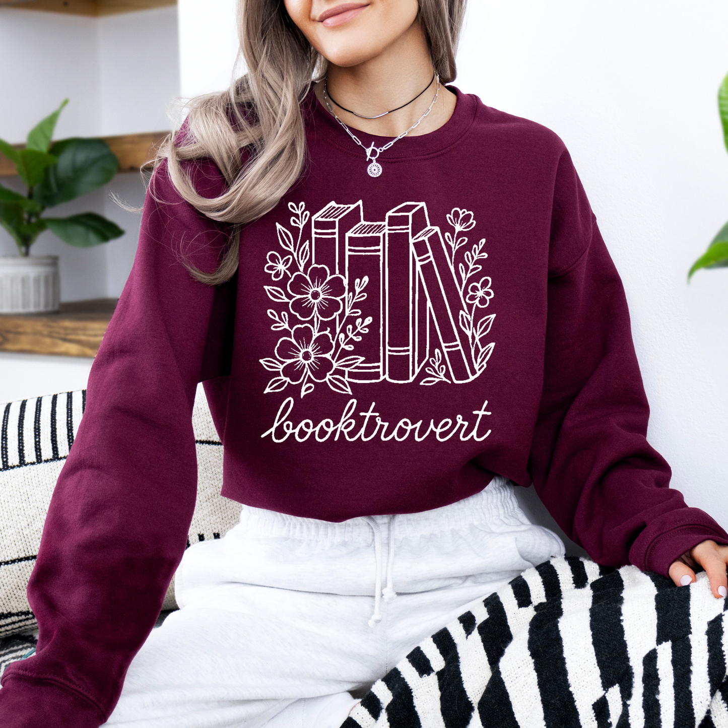 Person wearing a maroon sweatshirt with 'booktrovert' design, sitting on a zebra-patterned chair.