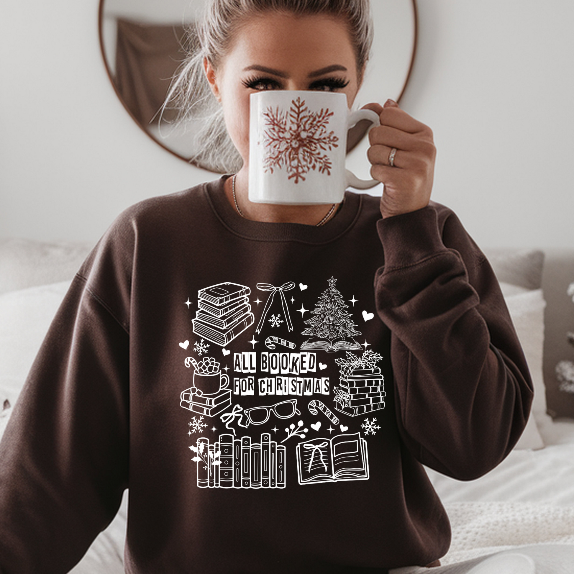 Person wearing a brown sweatshirt with Christmas-themed designs, holding a mug.