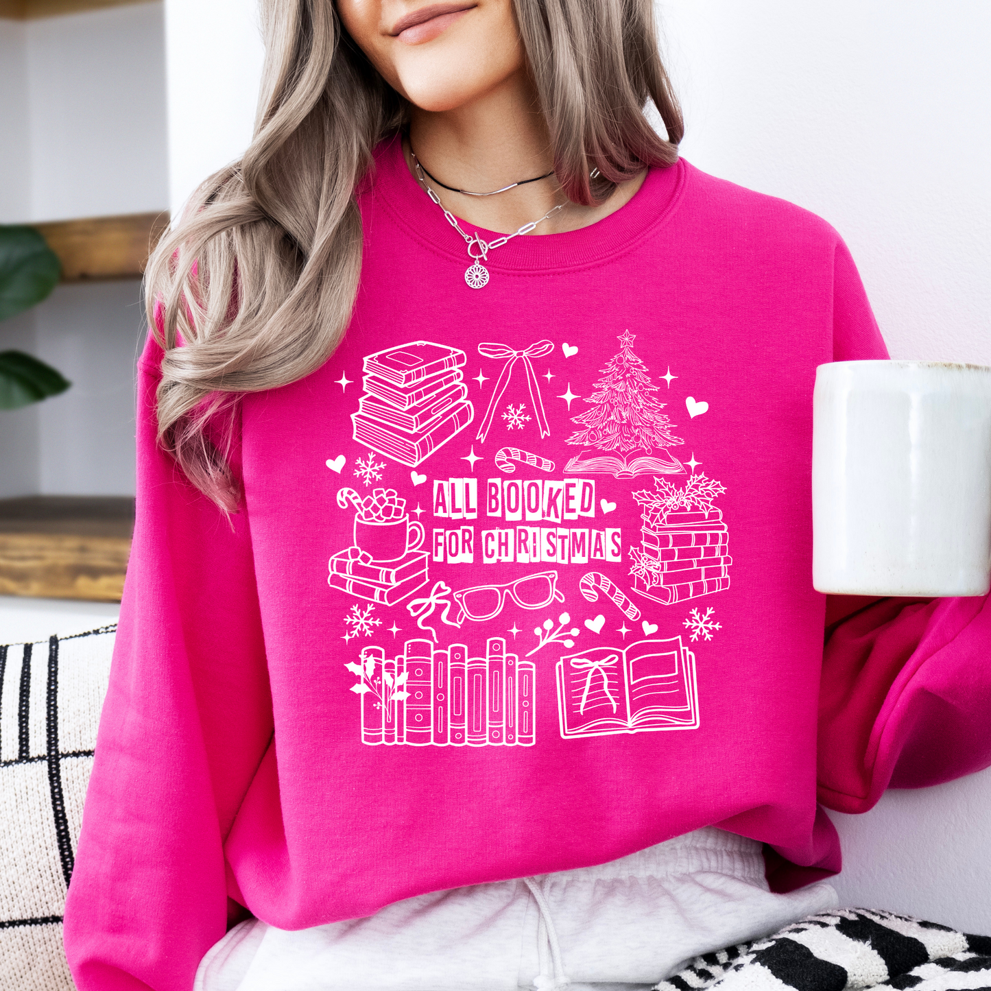 Person wearing a pink sweatshirt with Christmas-themed design, holding a mug.