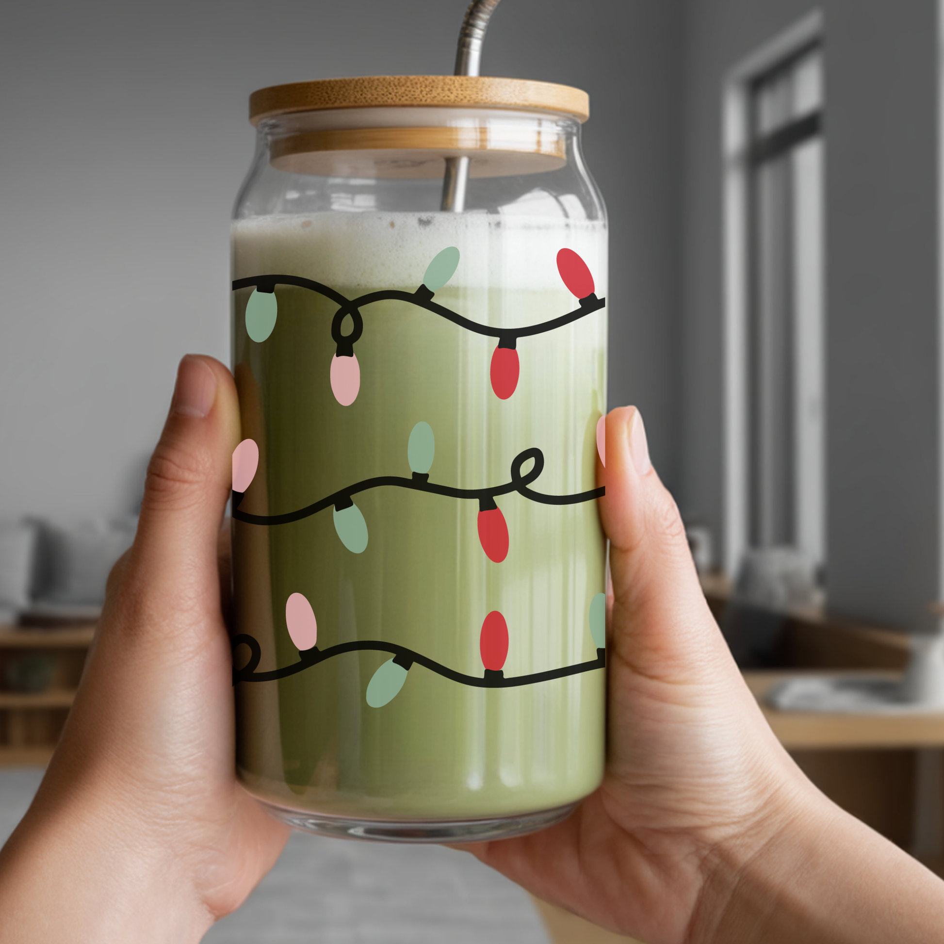 Glass jar with a wooden lid and straw, filled with a creamy liquid and Christmas lights design, held by a person indoors.