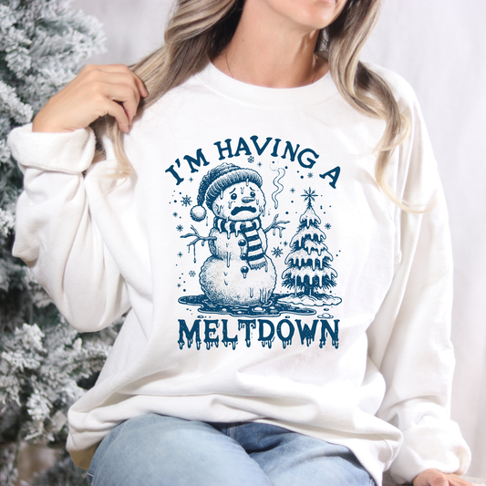 Person wearing a white sweatshirt with a blue snowman graphic and text in front of a Christmas tree.