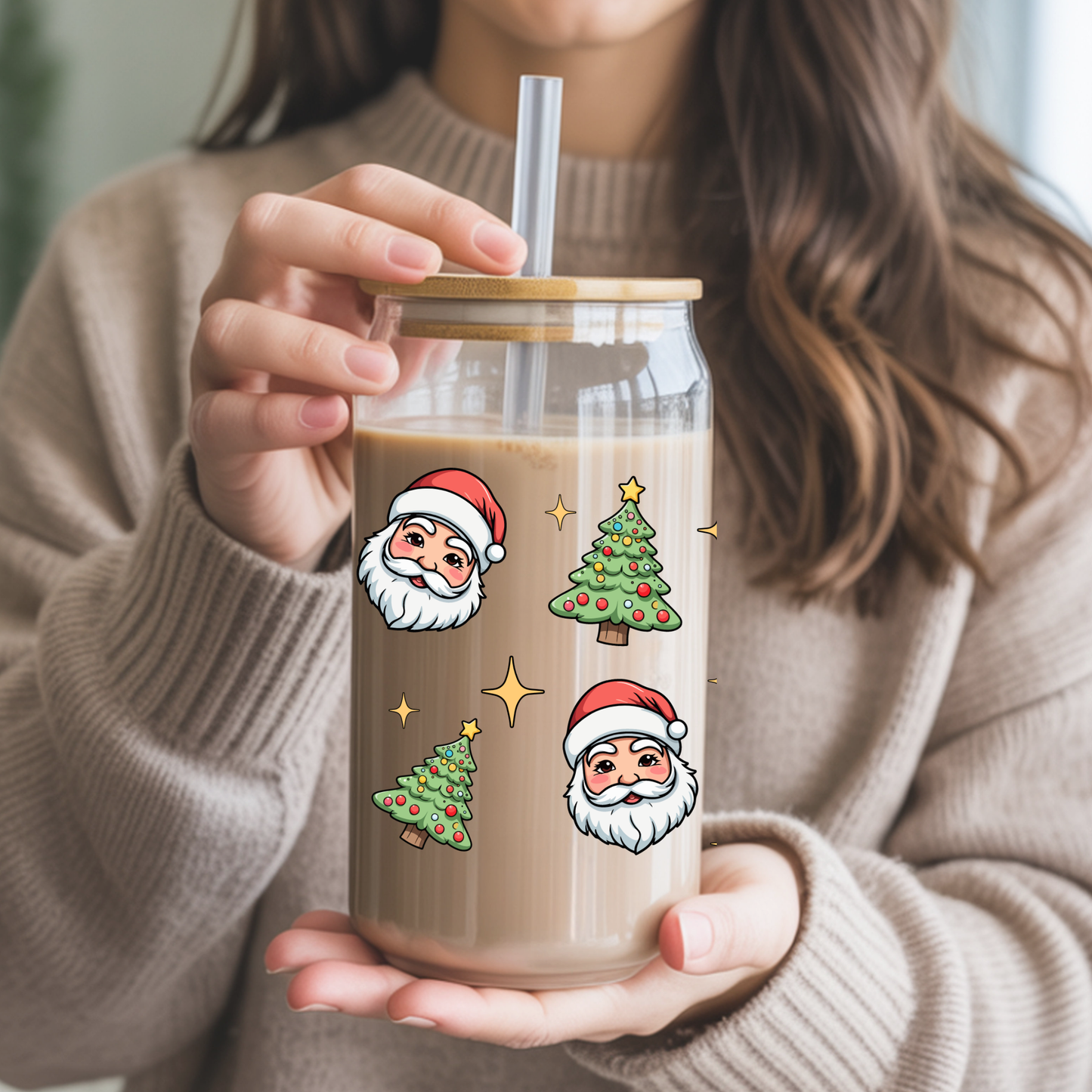 Person holding a glass mug with Christmas-themed illustrations and a straw.