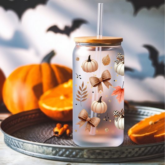 A frosted glass tumbler with a bamboo lid and clear straw, decorated with autumn motifs including pumpkins, leaves, and bows, displayed on a tray with pumpkins and bats in the background.