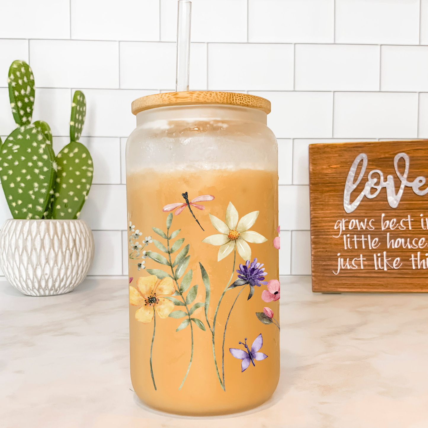 Decorative jar with floral design on a countertop with a cactus and 'love' sign in the background.