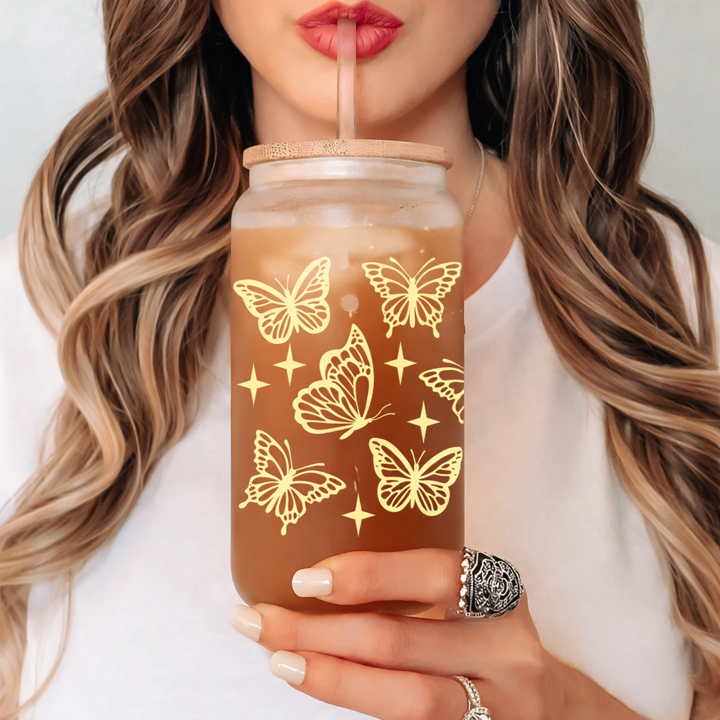 Person holding a glass with butterfly design and straw, wearing a ring.