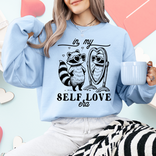 Person wearing a light blue sweatshirt with a raccoon and owl design and text, holding a mug.