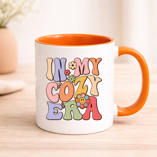 Mug with 'In My Cozy Era' text and colorful flowers on a wooden surface
