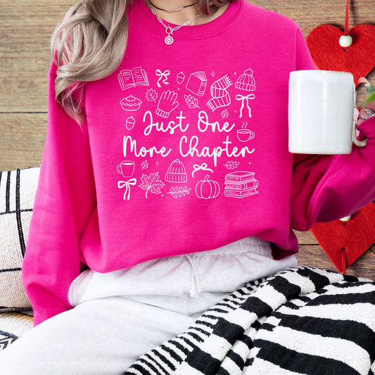 Person wearing a pink sweatshirt with 'Just One More Chapter' text and graphics, holding a mug.