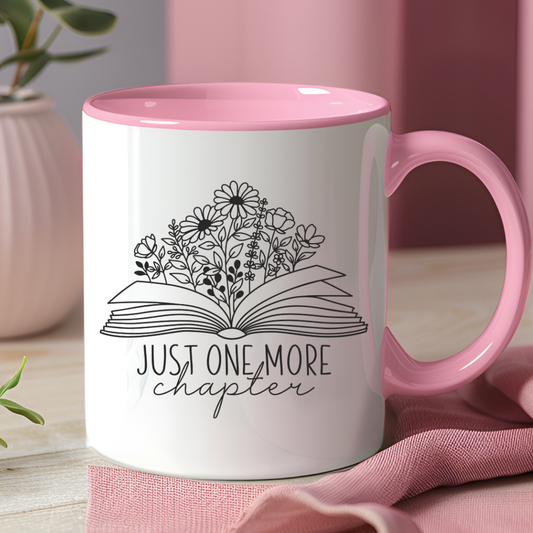 White mug with pink interior and handle, featuring a floral book design and 'Just One More Chapter' text.