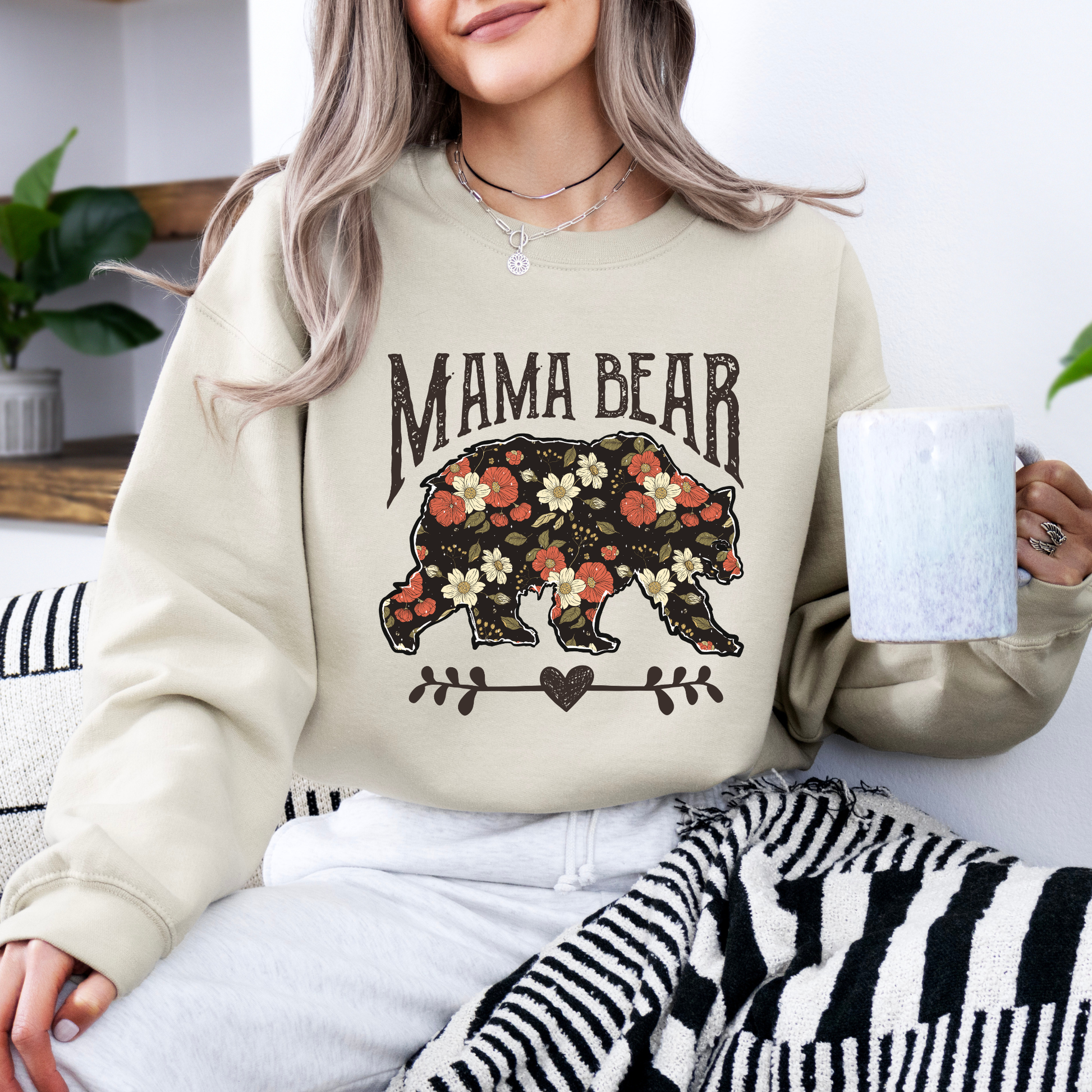 Person wearing a 'Mama Bear' sweatshirt with floral design, holding a mug.