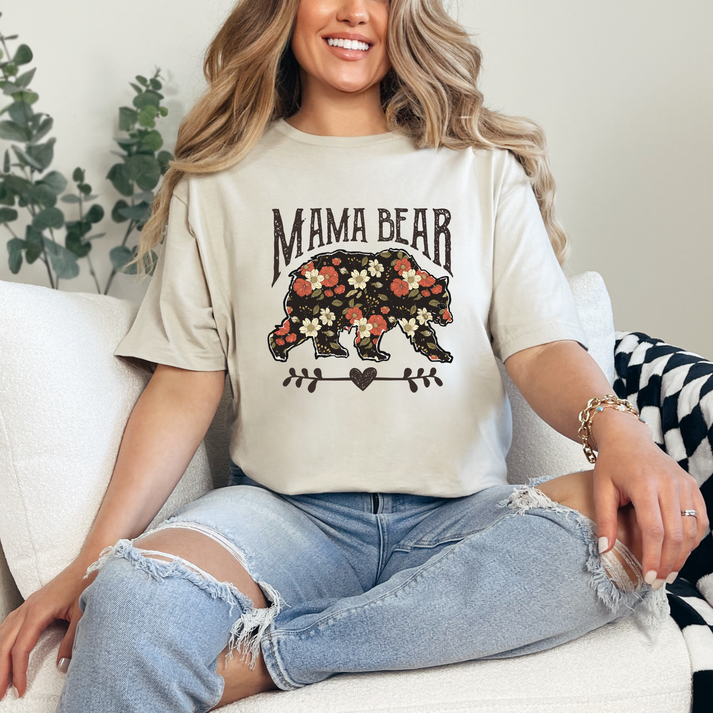 Woman wearing a 'Mama Bear' t-shirt with floral design sitting on a couch.
