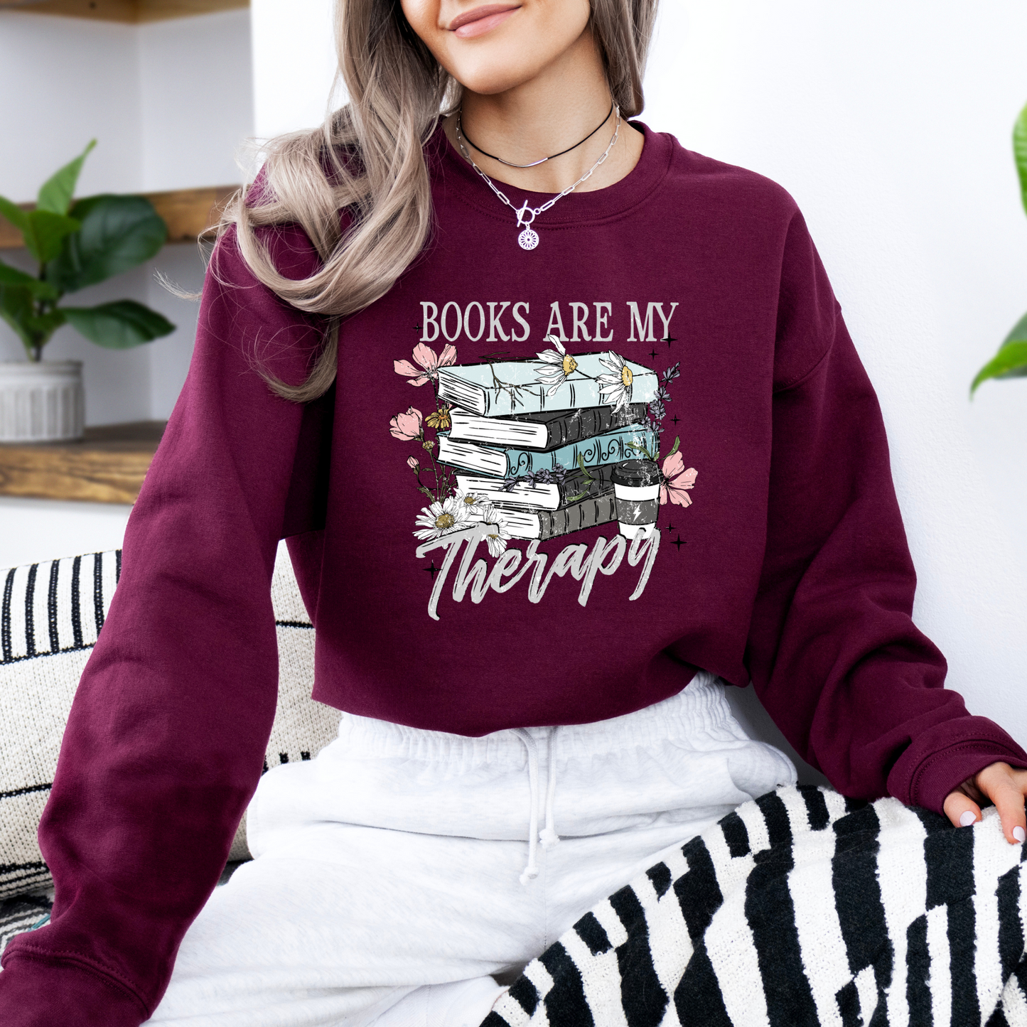 Person wearing a maroon sweatshirt with 'Books are my Therapy' design, sitting on a zebra-patterned chair.