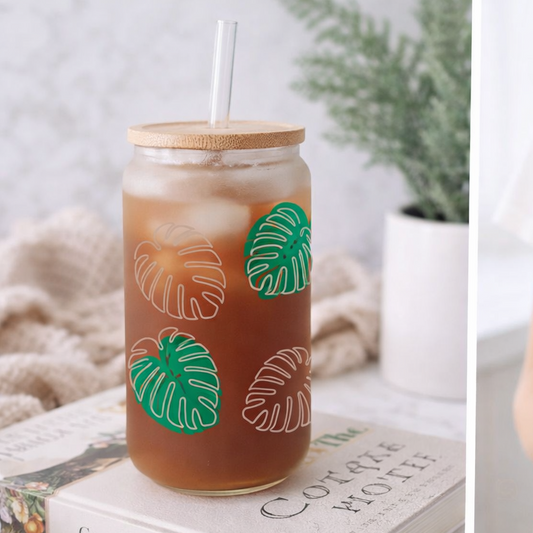 Mason jar with iced drink and leaf design held by a person, next to a book on a surface.
