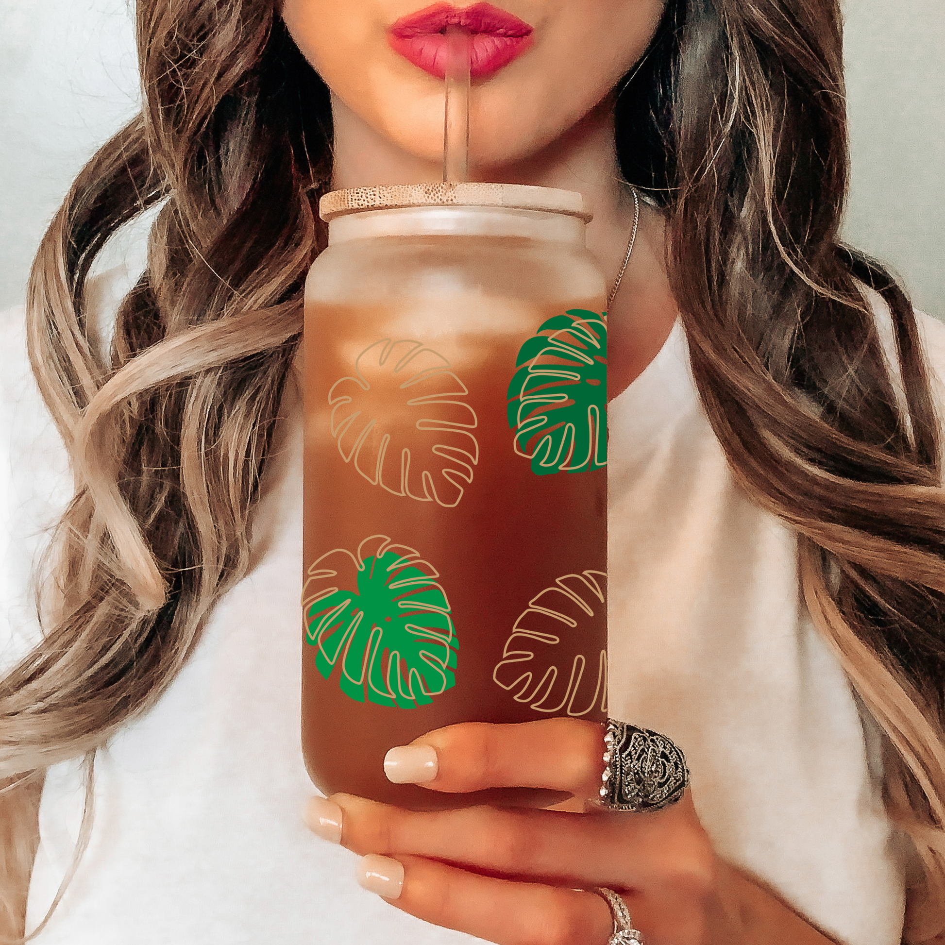 Person holding a tumbler with green leaf patterns, drinking from it.
