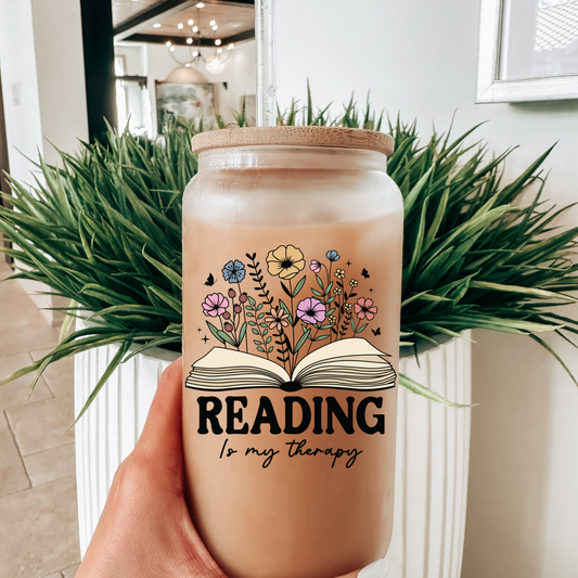 Tumbler with floral design and 'Reading is my therapy' text held in front of a plant.