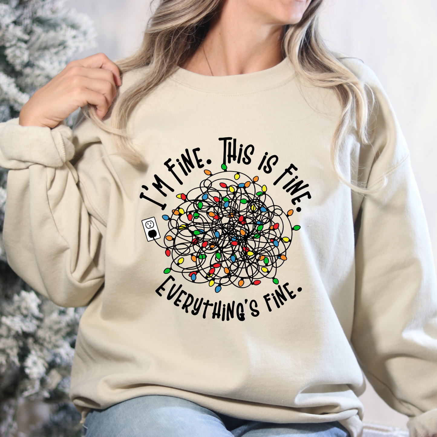 Beige sweatshirt with text and light bulb design worn by a person, against a blurred natural background.